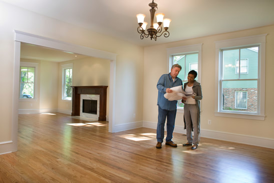 man and woman standing in new home holding plans